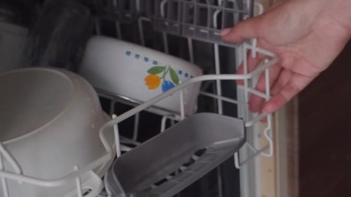 家庭主妇把脏盘子放在洗碗机里。女性双手在特写镜头中卸下洗碗机。家用现代家用电器。女人把装有脏盘子的顶