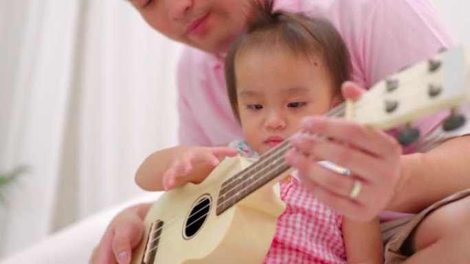 两岁的女儿和爸爸在沙发上弹吉他。