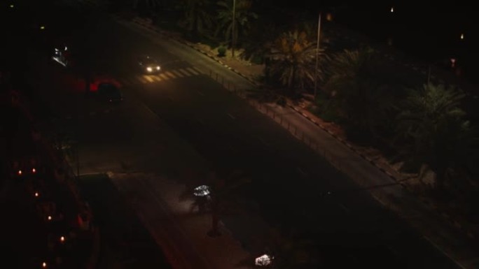 带有夜光大灯的汽车在夜间沿着度假小镇的道路行驶
