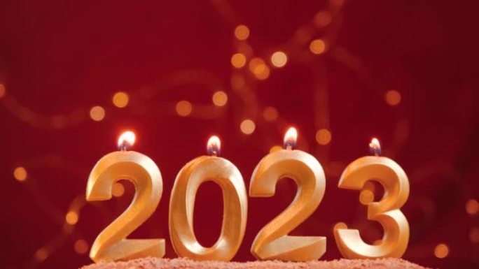 数字形状的金色蜡烛2023燃烧着火焰，卡在甜点蛋糕中。黄色的bokeh花环的灯光照在红色背景上。4k