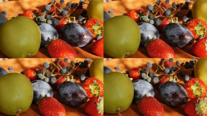 在日落时被阳光照亮的粘土盘中，五颜六色的新鲜水果和浆果。大草莓、青苹果和蓝梅配葡萄。水果和浆果成分