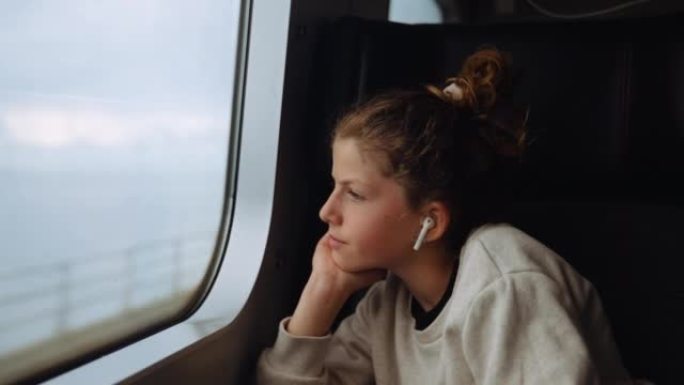 带耳塞的女孩坐在火车上看着窗外