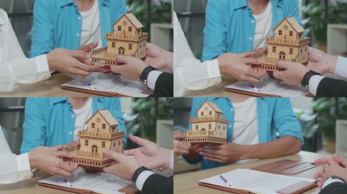 在签署购房合同文件后，一对夫妇的手从房地产经纪人那里收到房屋模型