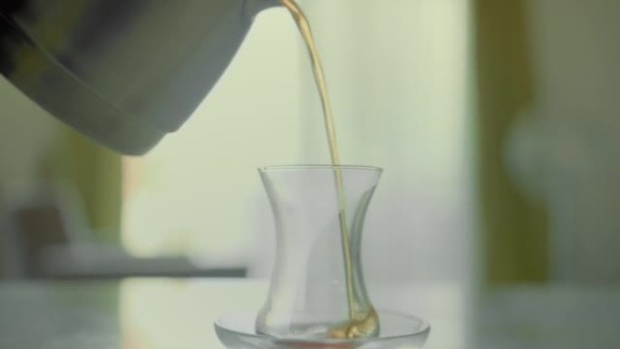 茶杯用茶托站在桌子上，窗户的背景，将冲泡的茶倒入玻璃杯中，特写