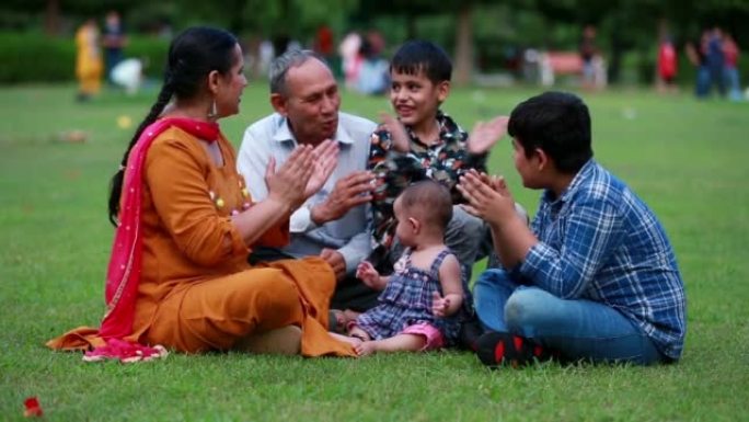 春天，快乐的印度家庭在公园户外坐着肖像。