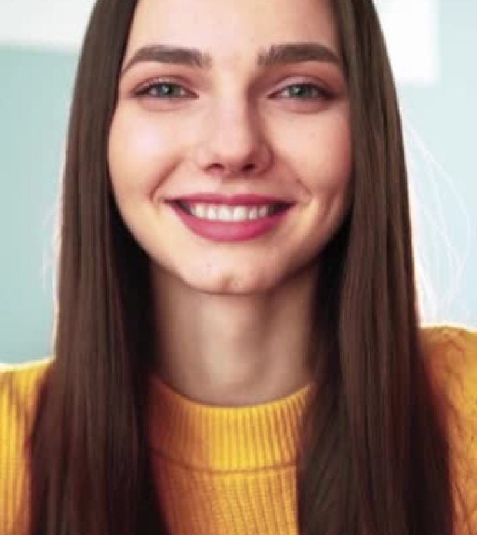 穿着黄色毛衣的垂直视频幸福的女人在网络摄像头上微笑着和她的追随者聊天。女性博客作者通过与观众的视频通