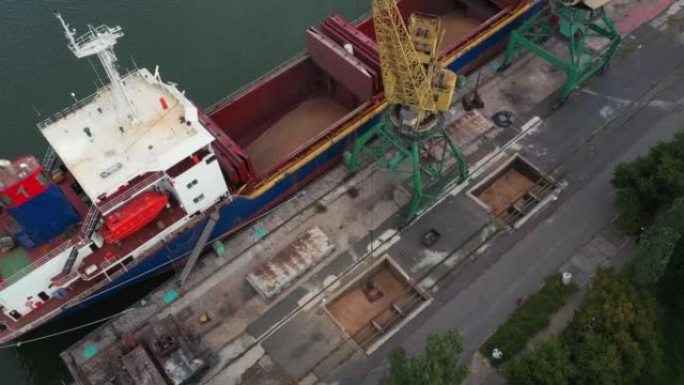 在海港的龙门起重机上，用双勺翻盖式抓斗从集装箱到船货舱的谷物转运。小麦从自卸车运水。商品运输。
