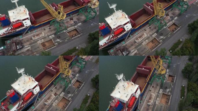 在海港的龙门起重机上，用双勺翻盖式抓斗从集装箱到船货舱的谷物转运。小麦从自卸车运水。商品运输。