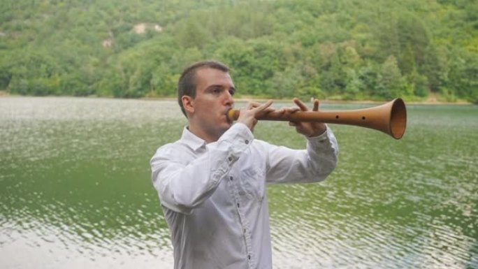 年轻的男音乐家站在湖边吹气时努力