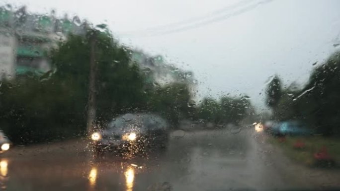 一辆停驶的汽车挡风玻璃上的雨滴。雨刷在工作。背景中模糊的汽车灯、街道和建筑物