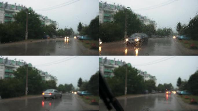 一辆停驶的汽车挡风玻璃上的雨滴。雨刷在工作。背景中模糊的汽车灯、街道和建筑物