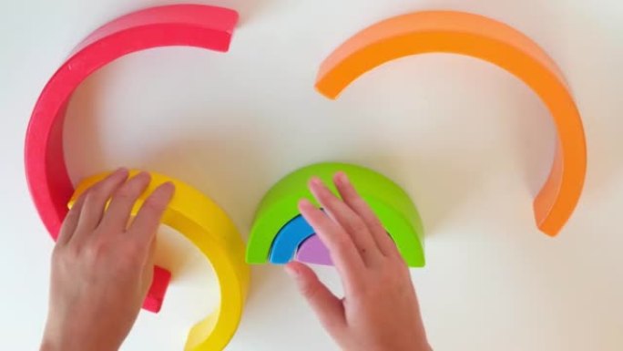 孩子们的手在白色桌子背景上玩木制玩具彩虹。手眼协调发展。集中。早期教育理念。感官游戏。精细的运动技能