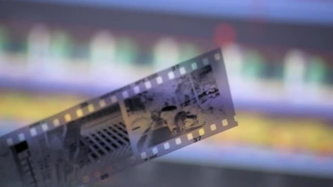 在监视器屏幕上的现代数字视频编辑软件正面的特写镜头中，男性手持旧胶片，显示了摄影和视频编辑剪辑的技术