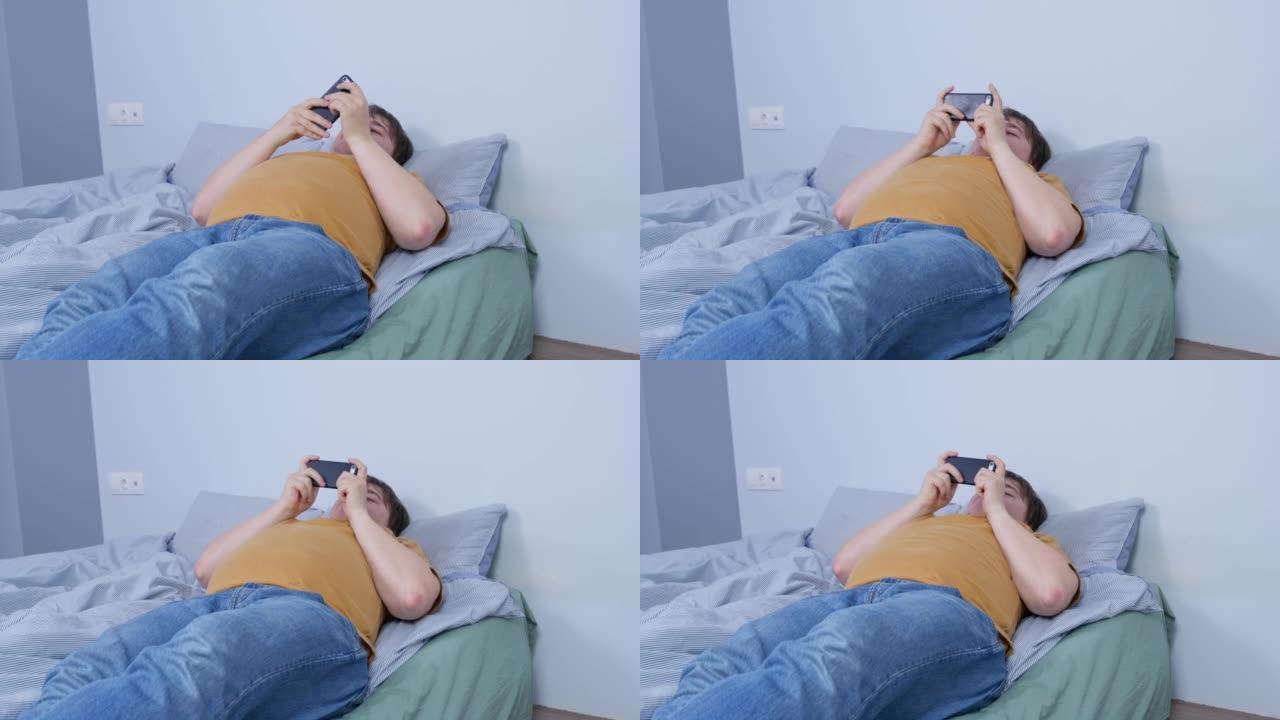 年轻人穿着衣服躺在床上，他拿出智能手机以防万一，开始玩在线手机游戏，阅读或观看流媒体频道，侧视图。