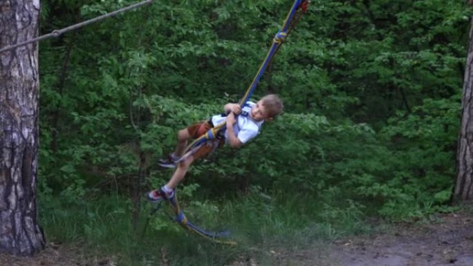 勇敢的男孩在安全支柱上下降了绳索公园的轨道。