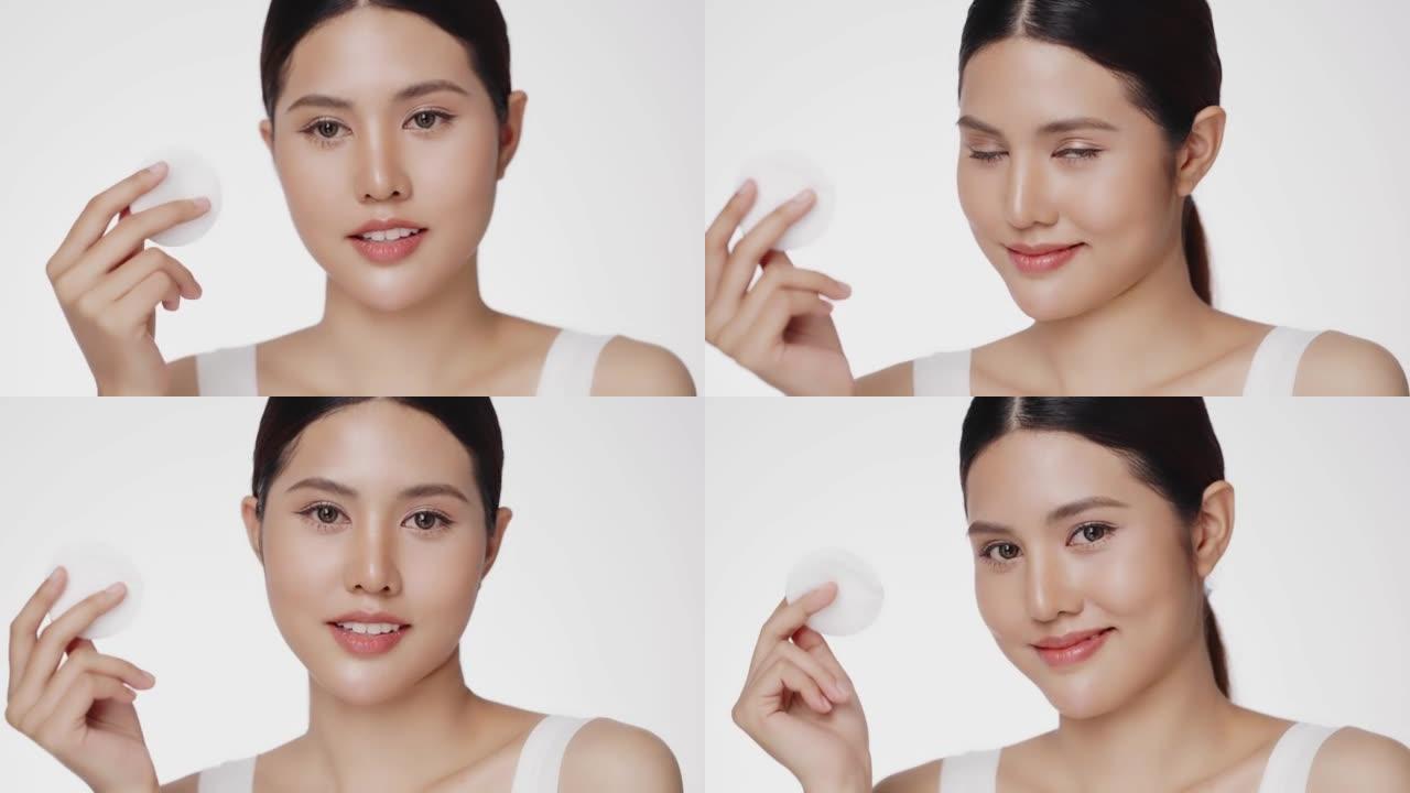 迷人美丽的年轻亚洲妇女清洁脸与棉垫隔离在白色背景。