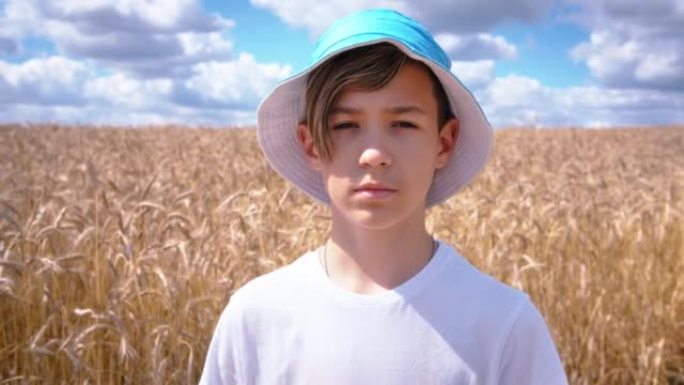 一个十几岁的男孩在麦田里看着相机的肖像，夏天阳光明媚的天气，移动的相机