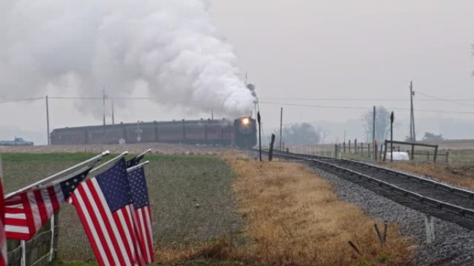 一列蒸汽旅客列车绕过弯道，吹着浓烟，在农田的篱笆上轻轻挥舞着美国国旗的长景