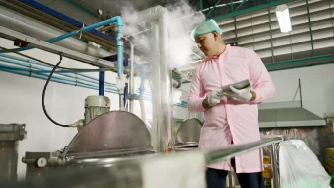 穿着发网和无菌服装的亚洲工程师或技术人员，通过瓶装果汁加工厂生产线中的平板电脑检查工作系统和温度大果
