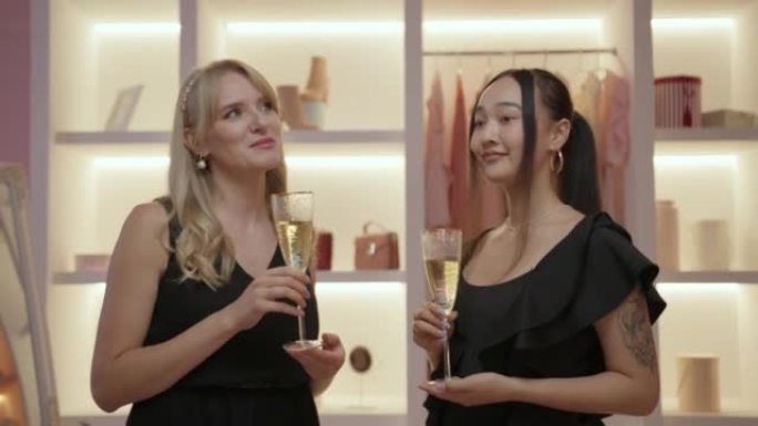 两个穿着黑色连衣裙的女性朋友站在衣柜里喝起泡酒聊天。为聚会做准备的女人。