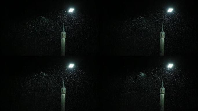 晚上大雨下的双发光二极管面板灯柱。雨滴在灯柱明亮的灯光下的中景。