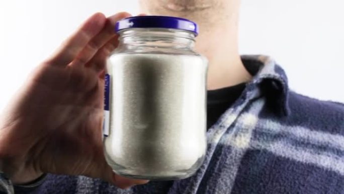 A man holds a glass jar with sugar crumbs. Sugar, 