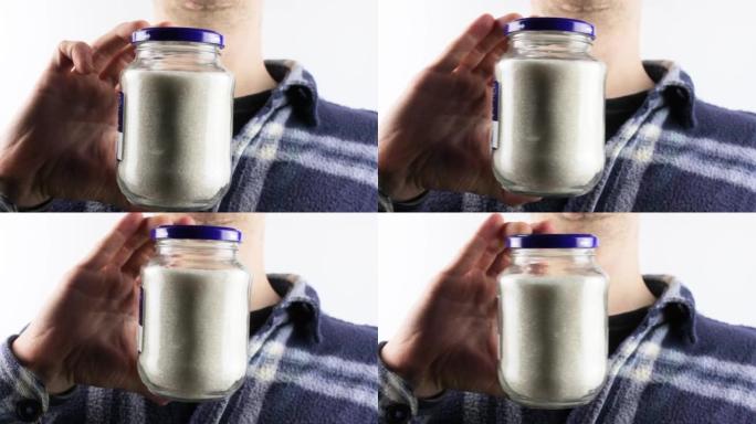 A man holds a glass jar with sugar crumbs. Sugar, 