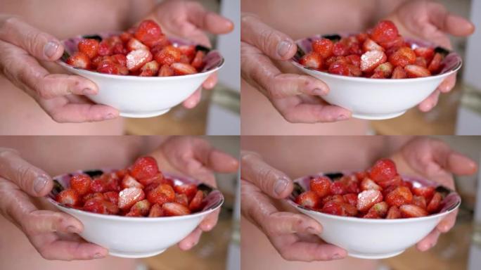 农夫手里拿着满满的玻璃碗红色的草莓在阳光下。特写。4K