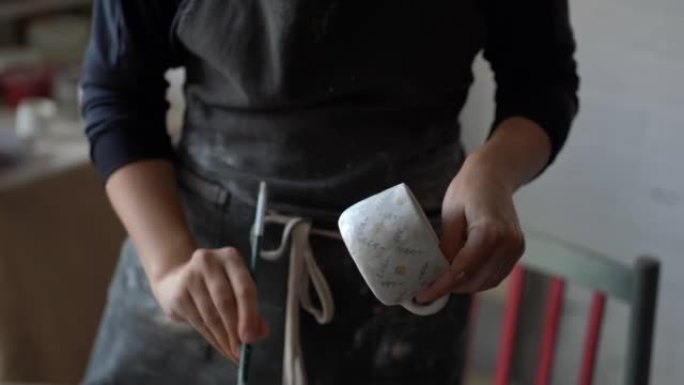 女工匠在模糊的背景上用画笔在工作室里画白色陶瓷杯