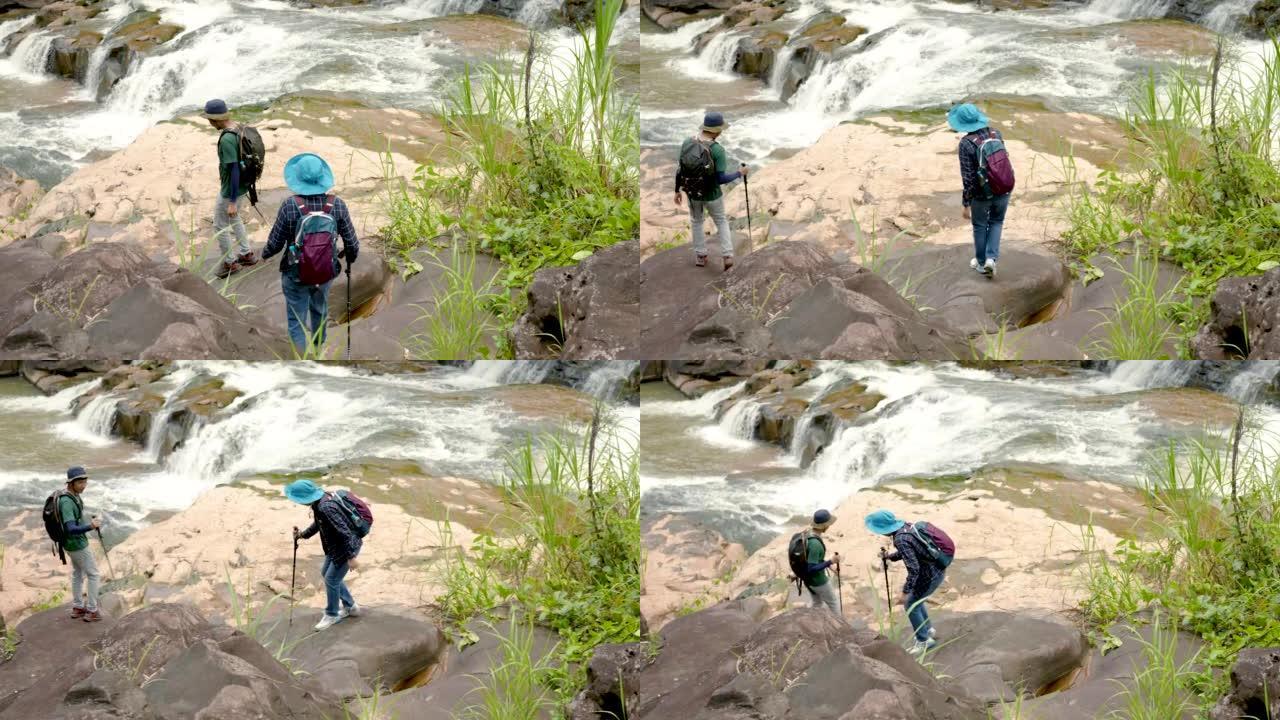 4K，年轻的亚洲夫妇，走下坡路，站在瀑布旁，看到瀑布沿着岩石凹槽流动，耳朵上容易，眼睛上容易，自然就