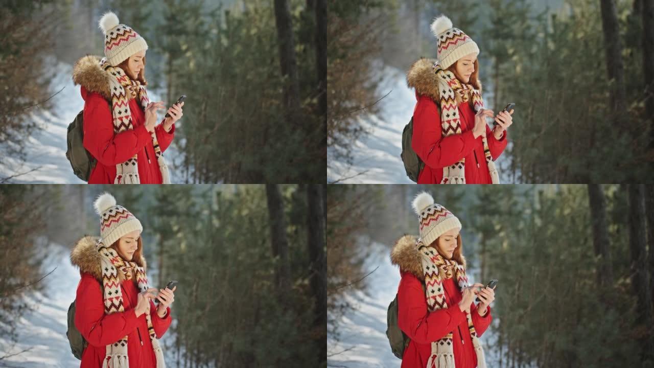 一个穿着红色夹克的红发女孩在冬天的夏日在森林公园里享受智能手机