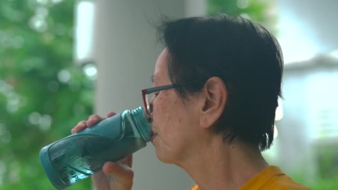 资深亚洲女性在家晨练后喝水。
