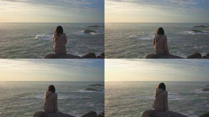 一个披着斗篷的女孩在日落时看着大海