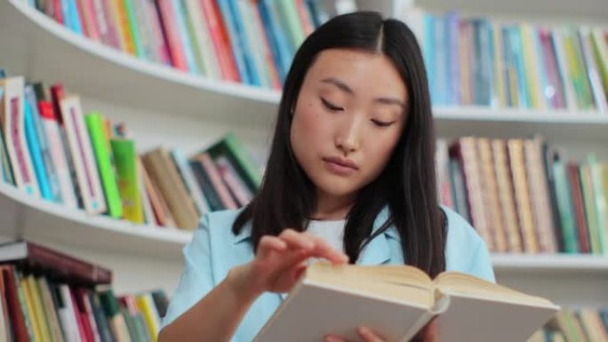 在大学图书馆书架附近的读书中关闭美丽的亚洲女孩。自我教育理念。