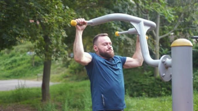 大胡子的男运动员在公园训练二头肌时努力