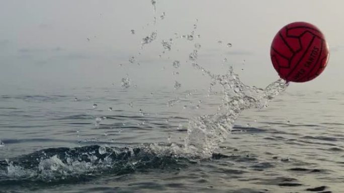 日落时分，球在大海的背景下飞出水面。球在水上的超慢动作。用高速电影摄影机拍摄。