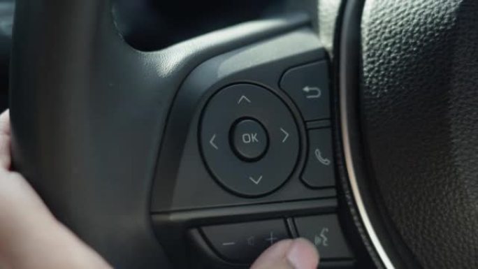 女人手指使用方向盘上的多媒体按钮来调节音量并在汽车中选择歌曲