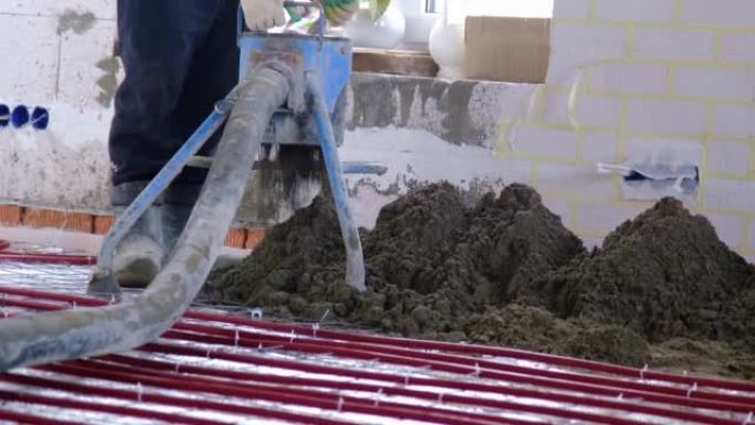 半干地板熨平板 -- 一名工人通过一个特殊的套筒铲出建筑混合物，用于在地板下加热管上固井和找平。慢动