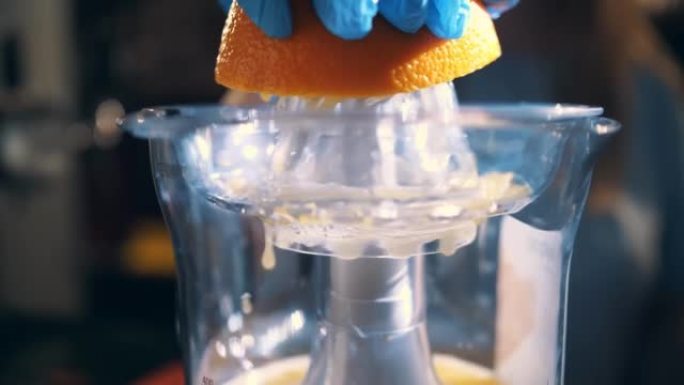 橙色新鲜。榨汁机。制作橙汁。柑橘汁。特写。戴着手套的手在电动榨汁机上从半个橙子中榨汁。