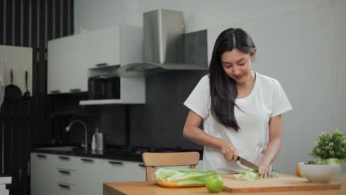 在减肥饮食中，女性在切菜板上切蔬菜和烹饪蔬菜沙拉。美丽的女人早上快乐地在厨房里做健康的早餐。饮食概念