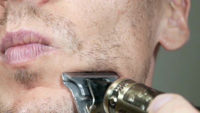 男人正在用坏的电动金属剃须刀或干剃须刀剪胡须。男人脸上胡须稀疏。头发生长问题。胡子上有脱发的人。胡子