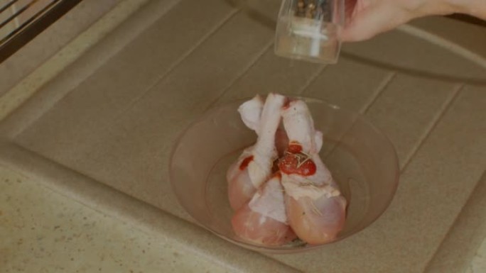 雌性的手在鸡腿上撒上胡椒，然后用番茄酱腌制。