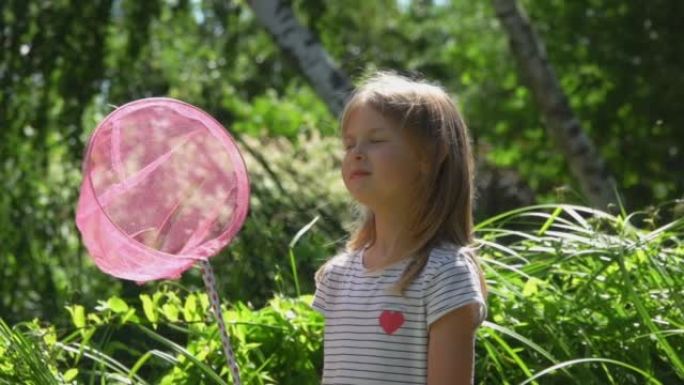 可爱的女孩带着粉红色的勺子网狩猎蝴蝶正在看相机