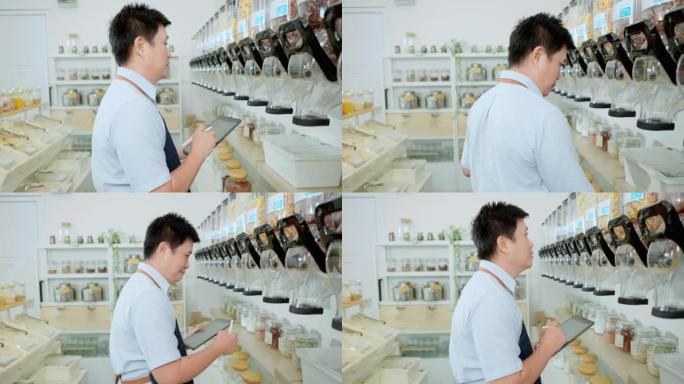 亚洲男士店主在出售给客户之前先检查容器中的有机产品库存，并在他的电子平板电脑设备上写下库存数量，再装
