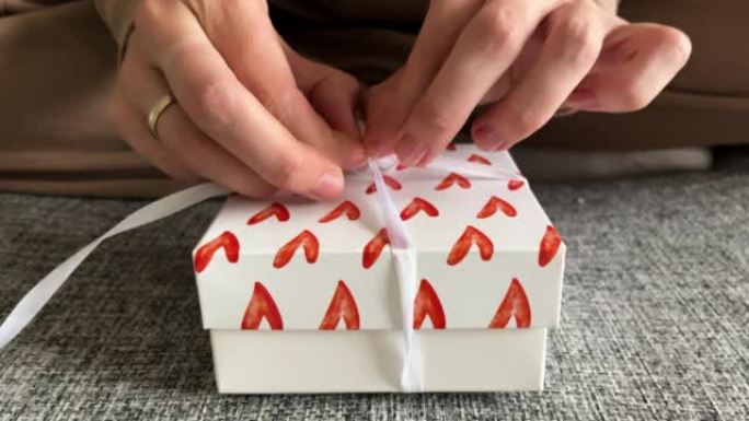女人用心在礼品盒上解开白色丝带。开箱礼物