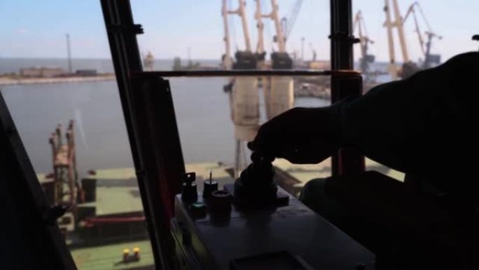 男子双手控制谷物码头操作员舱工作场所的操纵杆。工人通过在码头上移动行李箱机，用臂杆手柄控制从筒仓到散