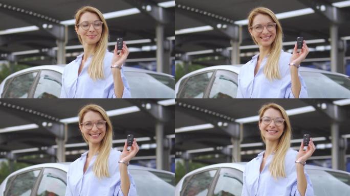 微笑的金发女人用新的外国汽车的钥匙吹牛，负担得起的积分