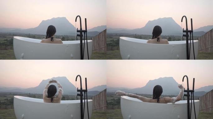 单身女性旅行者躺在户外浴缸上，在山景中放松
