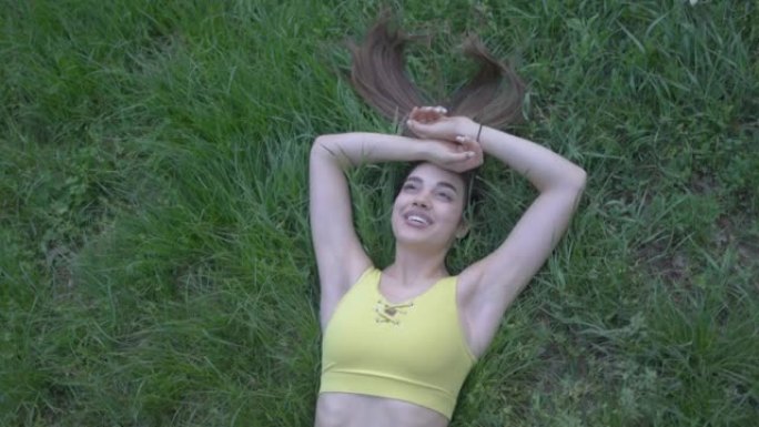 一个美丽的年轻女子，露出露齿的笑容，心满意足地躺在草地上，与大自然相连。