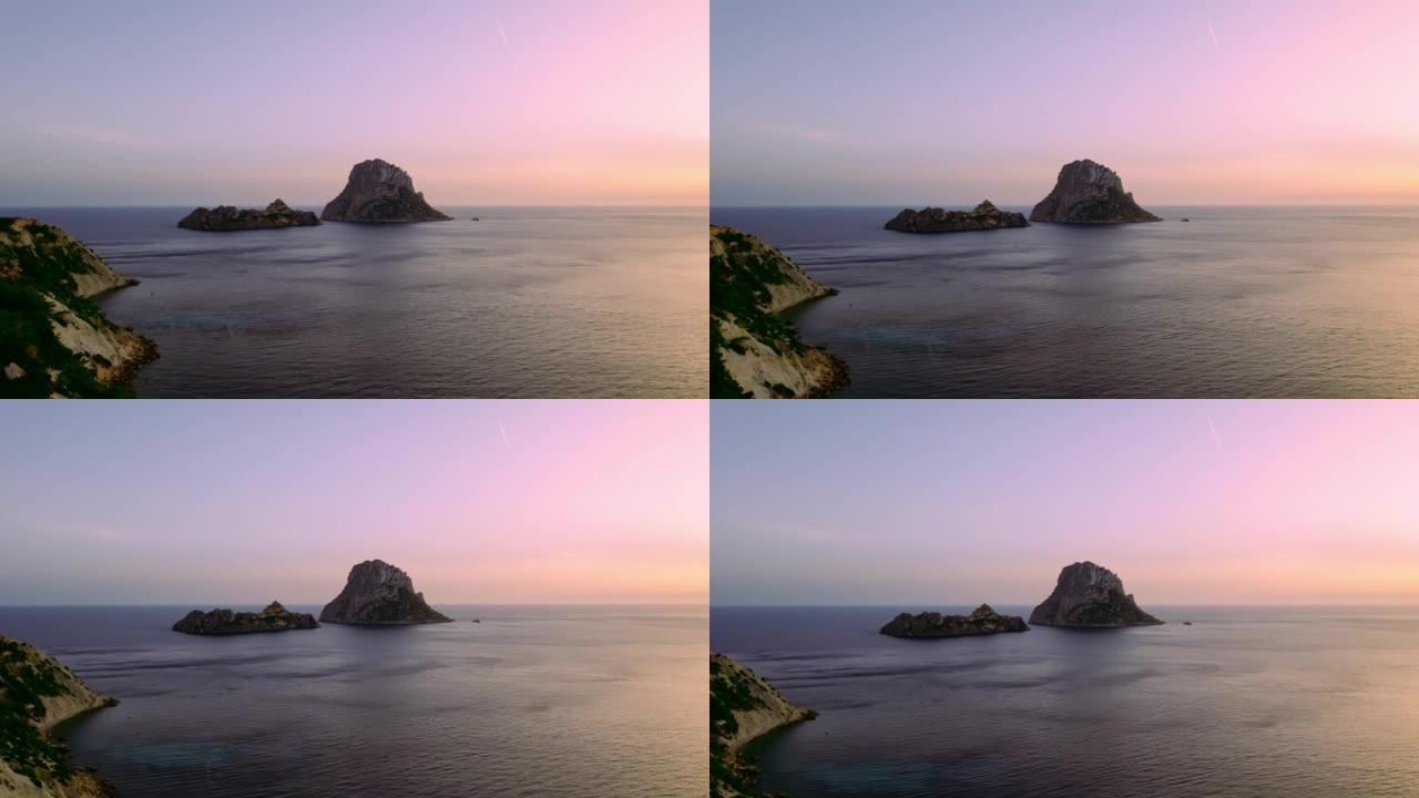 日落时Es Vedra Ibiza的鸟瞰图。展示海洋和晴朗的天空。电影4K